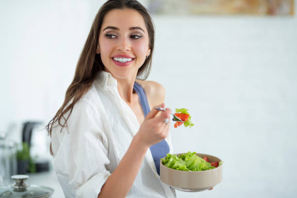 istock A beautiful young woman is feeling happy while eating a salad, standing in her kitchen 958988370
