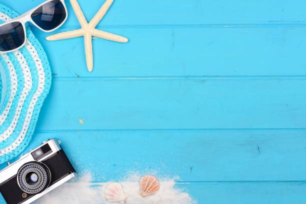 istock Beach travel concept side border with hat, sunglasses, shells, sand and camera on blue wood 958995414