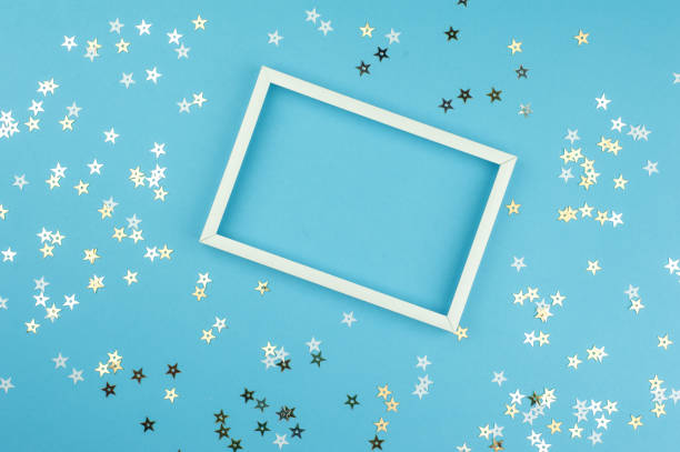 istock White picture frame and sequins stars on blue background. Top view, flat lay. Mockup for party or birthday invitation. 958995836