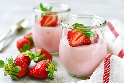 Natural strawberry yogurt with fresh berry and mint in a vintage glass jar on a light slate, stone or concrete background.