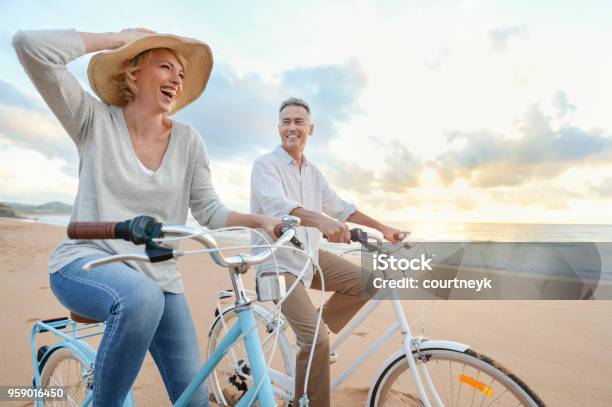 Coppia Matura In Bicicletta Sulla Spiaggia Al Tramonto O Allalba - Fotografie stock e altre immagini di Ciclismo