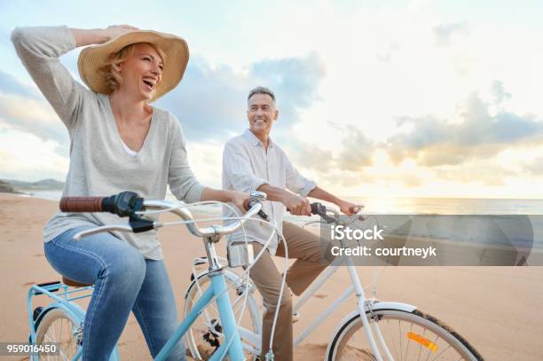 Mature Couple Cycling On The Beach At Sunset Or Sunrise Stock Photo - Download Image Now