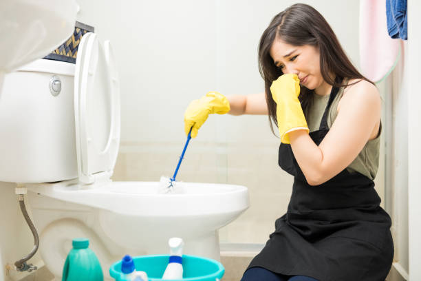 Woman with rubber glove is cleaning toilet bowl using brush Young woman covering nose to avoid bad smell while cleaning a smelly toilet bowl unpleasant smell stock pictures, royalty-free photos & images