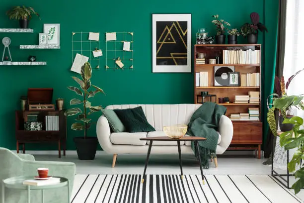 Modern design botanic living room interior with cozy beige sofa, antique furniture, home library, and green teal wall