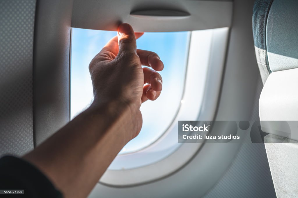 Man Adjusting the Blinds on an Airplane Window POV Personal perspective of a man adjusting the blinds on the inside of a commercial airplane window. The focus is on the hand. Airplane Stock Photo