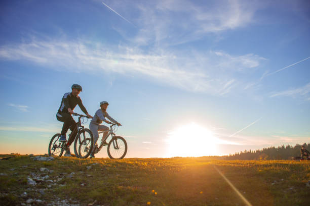 casal de bicicleta de montanha feliz ao ar livre se divertir juntos em um pôr do sol da tarde de verão - vitality clothing adventure mode of transport - fotografias e filmes do acervo