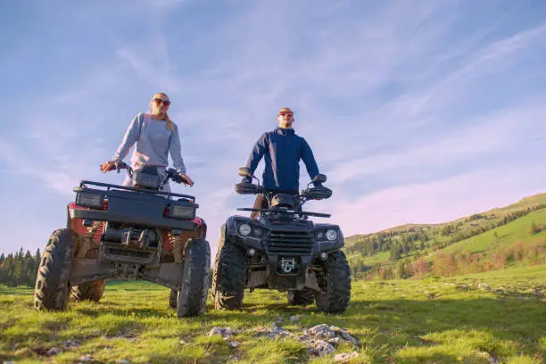 Beautiful couple is watching the sunset from the mountain sitting on atv quadbike.
