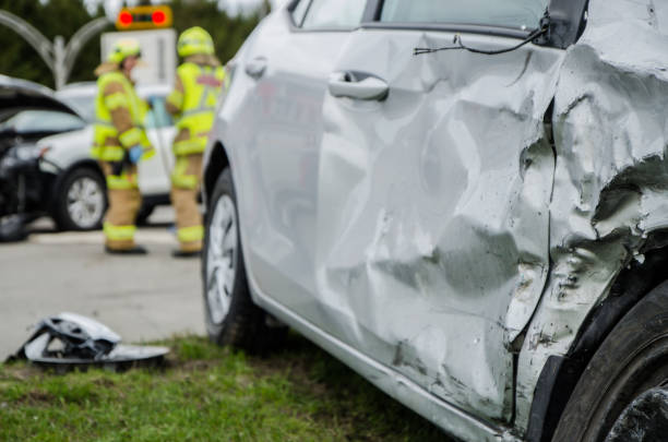 Close up on a car crashed with fireman in background Close up on a car crashed during an accident with  two firemen in background with firetruck during a day of summer car accident stock pictures, royalty-free photos & images