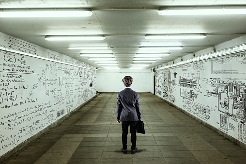 Businessman go through a tunnel with walls full of mathematical formulas and sketches.