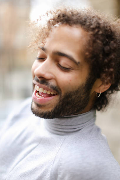 gros plan visage de personne du sexe masculin afro américaine avec des cheveux bouclé bruns et dents blanches - earring human face brown hair black hair photos et images de collection