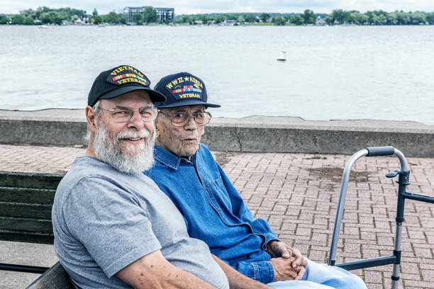 Two Generations of Senior Adult USA Military Veterans Sitting at the Lake Two generations of real person senior adult men USA military war veterans are sitting together sightseeing at the lake. On the right, a 95 year old United States Army World War II and Korean Conflict US Air Force military veteran - on the left, his son-in-law - a 67 year old US Navy Vietnam War military veteran. Canandaigua Lake, in the Finger Lakes region near Rochester, in western New York State.

They are both wearing inexpensive, non-branded, generic, souvenir shop replica military veteran commemorative baseball style caps.

NOTE: There are no official or authentic military uniform elements of any kind in this image - and no intent to portray anything other than proud and patriotic, authentic United States military war veterans. 90 plus years photos stock pictures, royalty-free photos & images