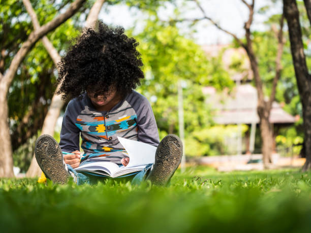 istock A little boy writing on notebook while sitting on green grass in a park 959070616