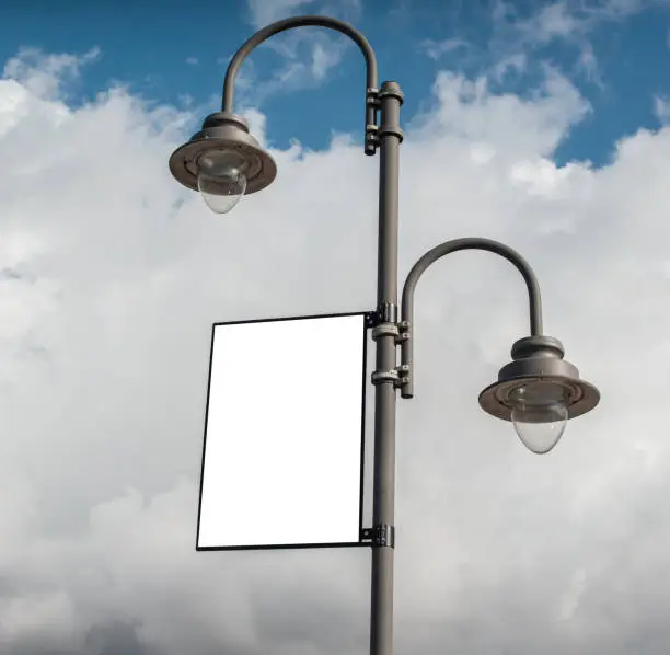 Photo of White blank rectangular billboard on a lamppost on a cloudy sky background