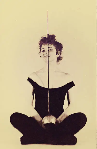 Vintage black and white photo from the sixties of the twentieth century featuring a young woman sitting with a fencing sword .