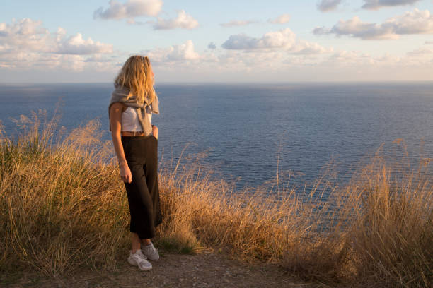 istock Young woman looks out to sea and lofty clouds 959095930
