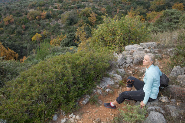 Woman hiker rests on trail, wearing knee brace She is in profile and the rocky trail leads away from her blue and green braces stock pictures, royalty-free photos & images