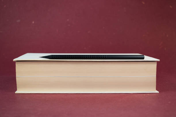 istock White hardcover book with black pencil on red background. 959109214