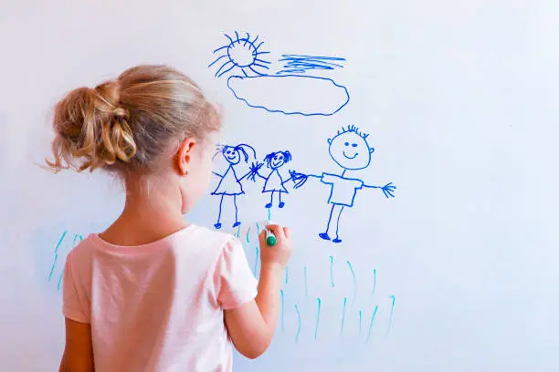 Little girl draws  family with marker on a white board: mom, dad and baby holding hands.