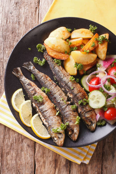 istock Fried sardines with potatoes and fresh vegetable salad close-up. vertical top view 959109860