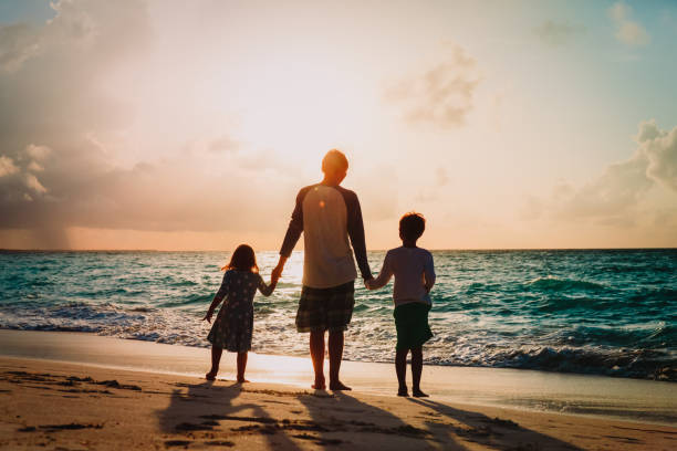 istock father and two kids walking on beach at sunset 959109952