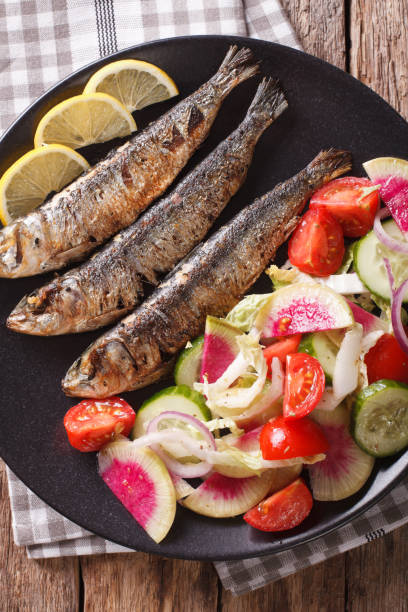 istock Mediterranean food: grilled sardines with fresh vegetable salad close-up. vertical top view 959110236