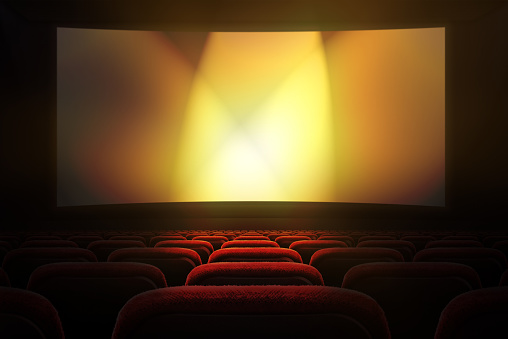 Movie theater with row of red seats and projection screen with golden lights in the background