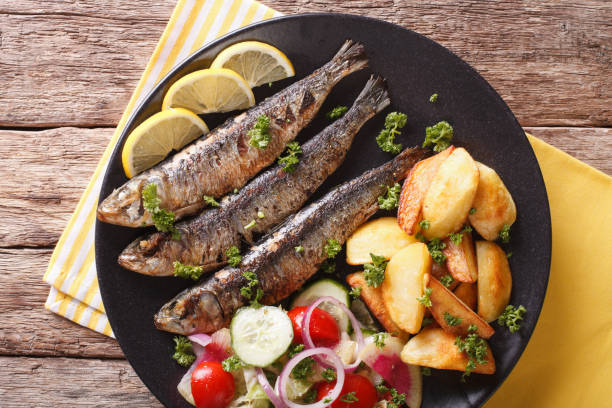istock Fried sardines with potatoes and fresh vegetable salad close-up. Horizontal top view 959115784