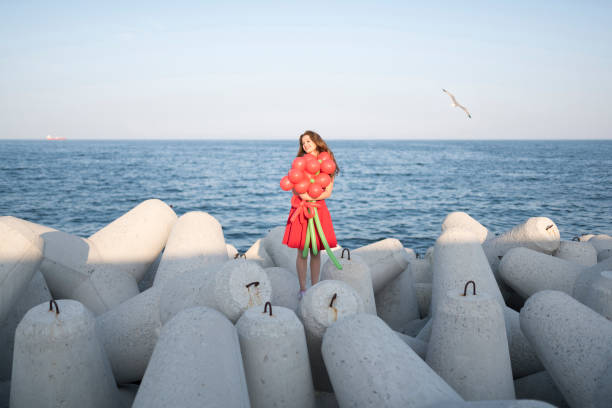 海のそばの大きなバルーン花束と赤で日夢を見る女性