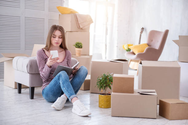 Pretty young woman checking number of removers Need assistance. Charming young woman sitting on the floor and checking the number of removers company before moving out of the house independence document agreement contract stock pictures, royalty-free photos & images