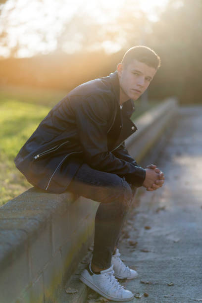 istock Stylish young man in leather jacket looking at camera, sitting in a park 959125742