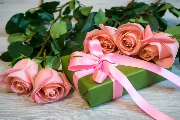 Pink roses and gift box in green wrapping paper with pink ribbon on wooden background