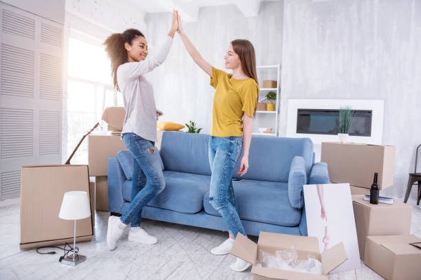 Upbeat young girls high-fiving each other in new flat Well done. Happy young girls high-fiving each other and exchanging smiles, having finished with unpacking plan for today roommate stock pictures, royalty-free photos & images
