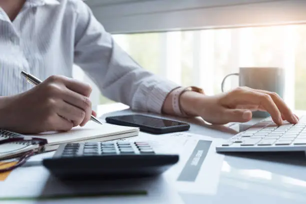 Photo of Business women using computer and calculator during note some data on notepad for calculate financial at home office