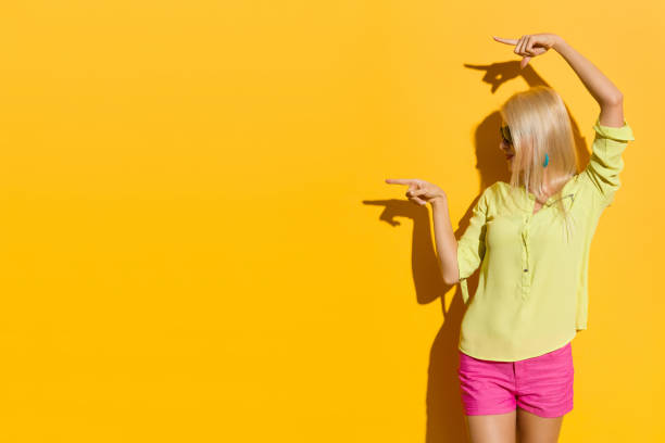 istock Smiling Young Blond Woman Is Pointing At Copy Space And Looking Away. Side View. 959148818