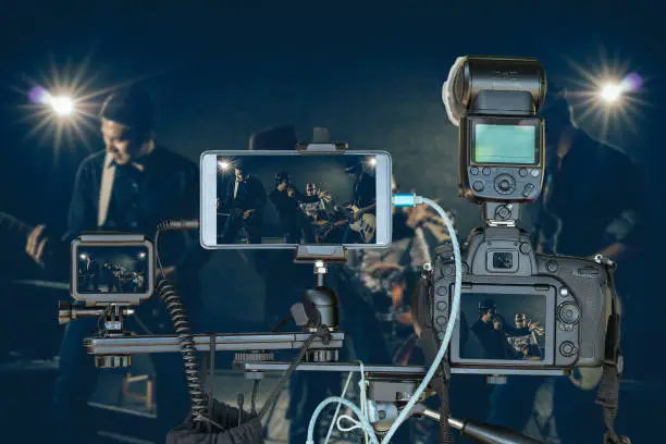 Photo of Professional set of camera with smart mobile phone and action camera on tripod over Musician band holding the microphone singing a song and playing music instrument,Live Streaming for musical concept