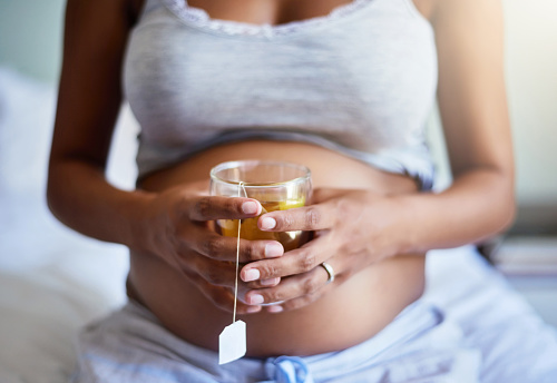 Cropped shot of a pregnant woman relaxing at home with a glass of tea