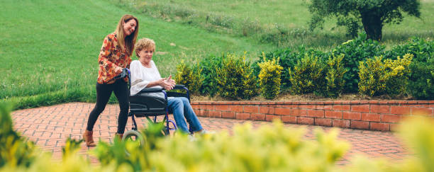 Woman carrying her mother in a wheelchair Young woman carrying her mother in a wheelchair through the garden elderberry photos stock pictures, royalty-free photos & images