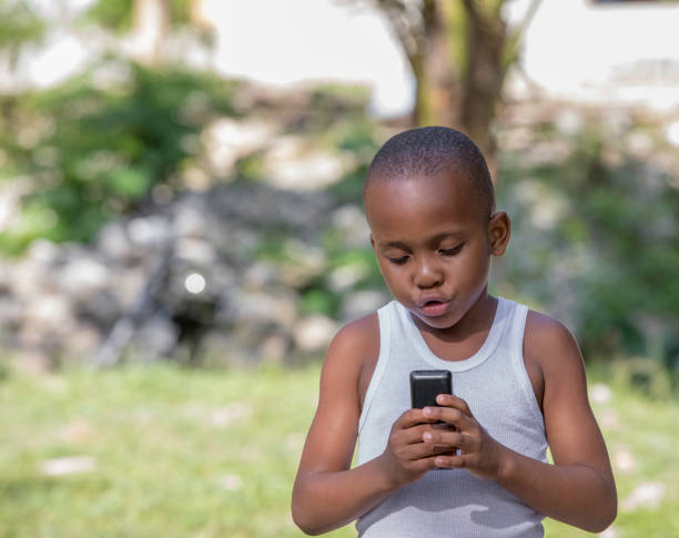 Young Jamaican boy with a cell phone A Jamaican is standing outside looking at a cell phone. Shot with a Canon 5D Mark lV. ariel west bank stock pictures, royalty-free photos & images