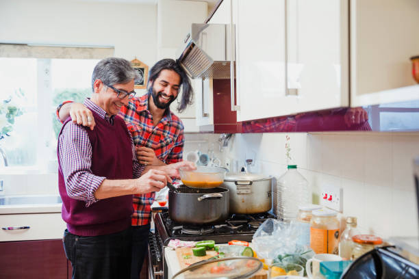 Accompanying Dad While he Cooks Mid adult man is looking over his father's shoulder as he prepares a curry at home. pakistani ethnicity stock pictures, royalty-free photos & images