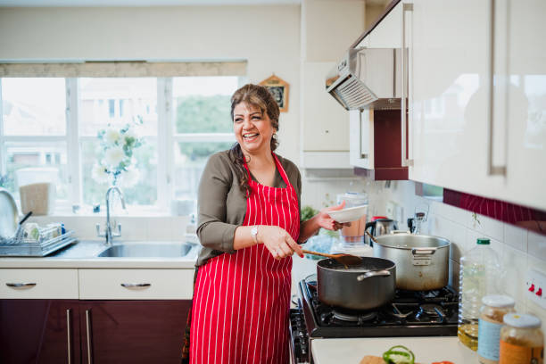 Mature Woman Enjoying Cooking at Home Mature woman is talking and laughing with someone out of the frame while she makes dinner at the cooker. stay at home saying stock pictures, royalty-free photos & images