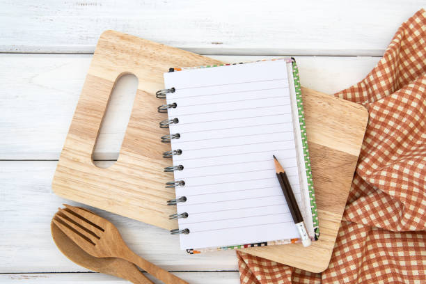 istock lined book notepad paper on chopping cutting board and tablecloth with wooden fork and spoon on white table , recipes food  for a healthy habits shot note background concept 959176758