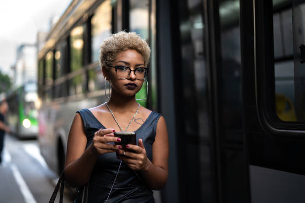 jovem mulher usando mobile espera o ônibus - candid women portrait human face - fotografias e filmes do acervo