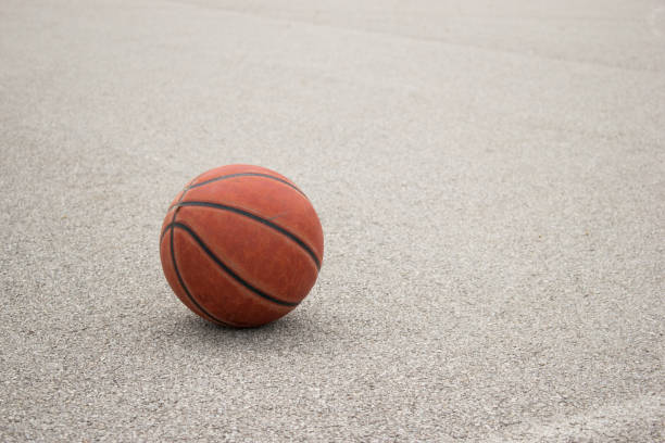 istock Used orange leather basketball on grey asphalt background. 959181360