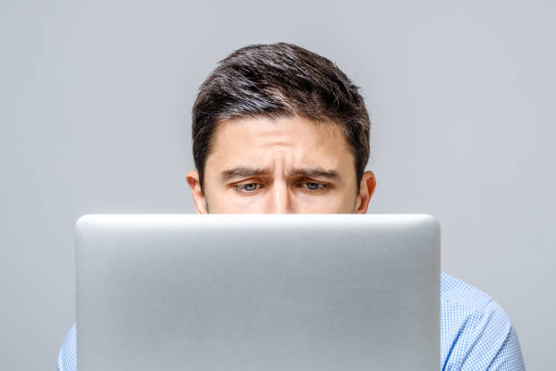 istock Pensive sad man sitting at the table with laptop over gray background 959190326