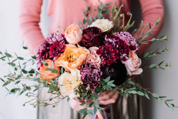 femme de fleuriste très agréable tenant un bouquet de fleurs belle floraison colorée de roses fraîches, pivoine, renoncule, tulipes, oeillets sur le fond du mur gris - arrangement flower head flower blossom photos et images de collection