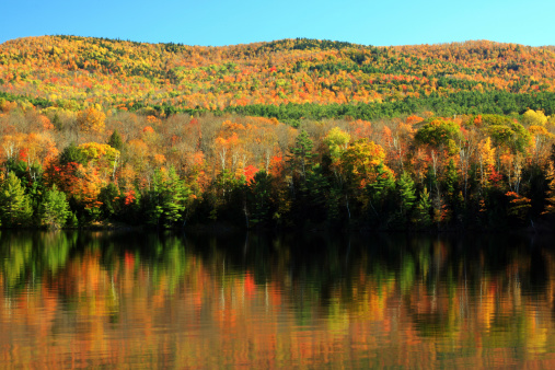 Image of Cascading falls drop off cliff edge into body of water during colorful peak fall