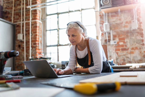 Senior woman using a laptop in a workshop Confident senior woman working in workshop one senior woman only stock pictures, royalty-free photos & images