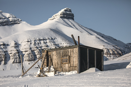 Photo of a hunting cabin by Billefjord, Svalbard and snow capped mountains in the background.