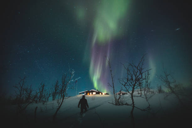 Man and Northern Lights over Riksgransen, Sweden A figure walks towards a cabin under the beautiful Northern lights in the night sky above Riksgransen, Sweden. norrbotten province stock pictures, royalty-free photos & images