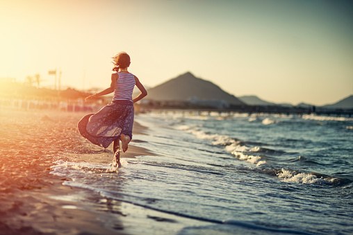 Portrait of a little girl running on the beach on a windy summer sunset.\nNikon D800